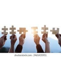 Several hands hold up large puzzle pieces against a bright sky, symbolizing teamwork and collaboration.